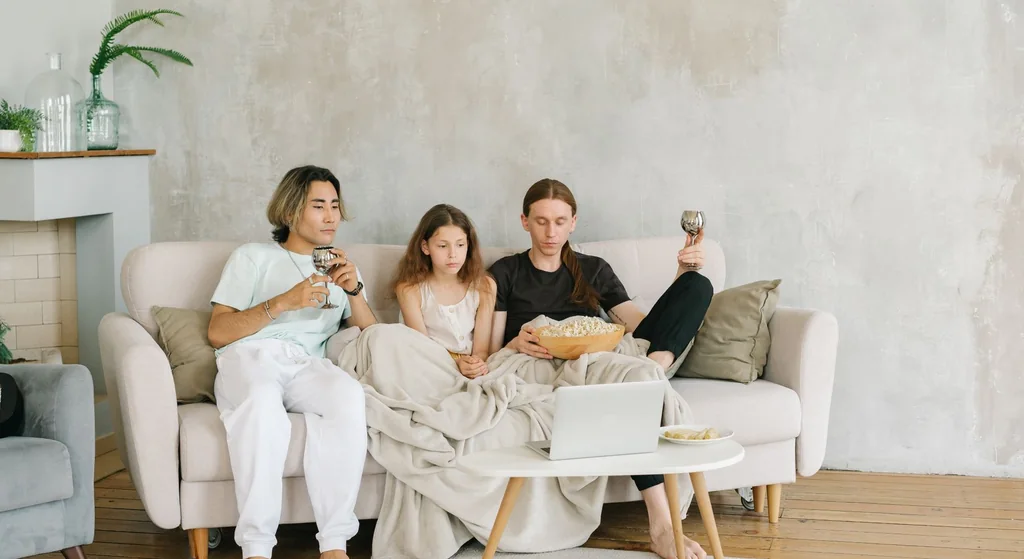 Stock photograph: three people sitting together on a sofa in a bright living room, watching a laptop open on a low table